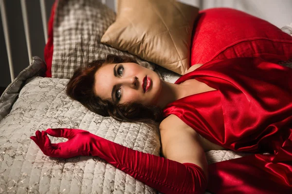 Sensual brunette in a red dress lying on the bed — Stock Photo, Image