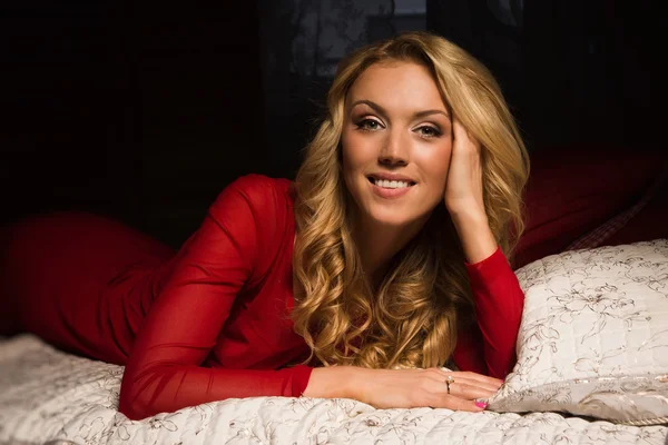 Sensuell blond i en röd klänning som ligger på sängen — Stockfoto