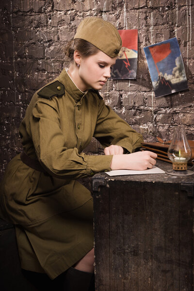 Soviet female soldier in uniform of World War II writes a letter