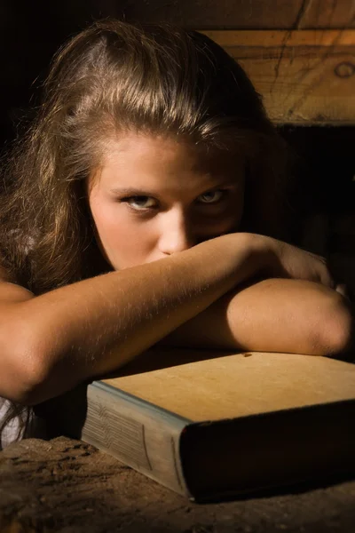 Jeune fille assise avec vieux livre dans un intérieur sombre — Photo