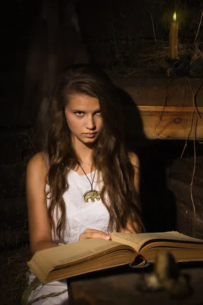 Jovem sentada com livro velho em um interior escuro — Fotografia de Stock