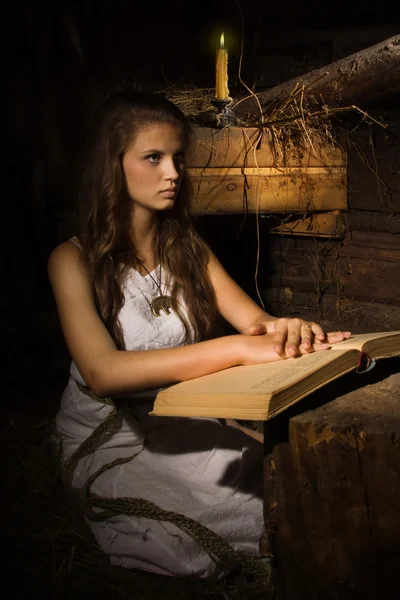 Jeune fille assise avec vieux livre dans un intérieur sombre — Photo