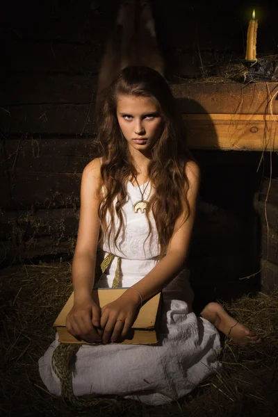 Giovane ragazza seduta con vecchio libro in un interno buio — Foto Stock