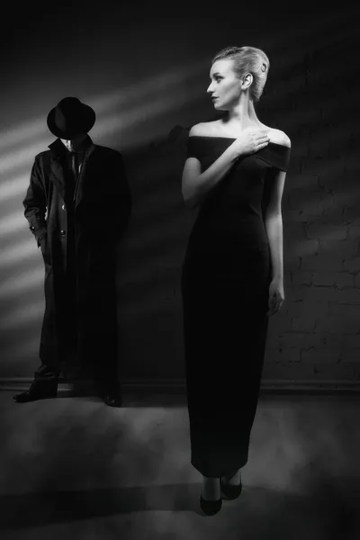 Donna con un lungo vestito nero e un uomo con un impermeabile e un cappello — Foto Stock