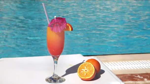 Orangencocktail mit Sonnenschirm und Stroh in der Nähe des Schwimmbades — Stockvideo