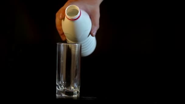 Mano con botella de leche que fluye en el vaso aislado sobre fondo negro — Vídeos de Stock