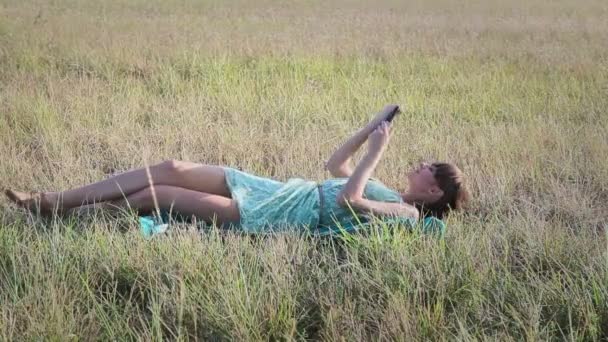 Jovem mulher navegando na Internet com tablet deitado na grama — Vídeo de Stock