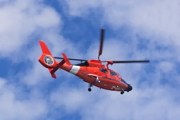 Kırmızı kurtarma helikopteri mavi gökyüzünde ilerliyor.