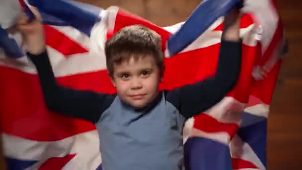 Concepto de fanático deportivo. Un niño pequeño con una bandera británica sobre un fondo de madera. Un niño de siete años sacude la bandera de Inglaterra y es un apoyo para el concepto del equipo de fútbol. Imágenes de alta calidad 4k — Vídeo de stock