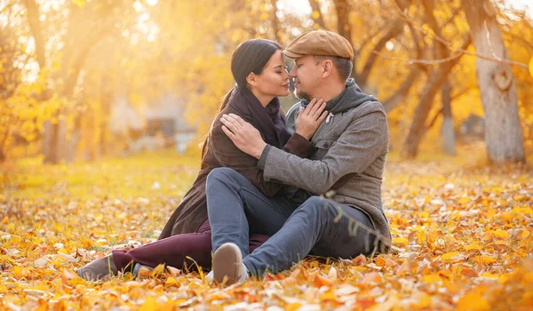 Romantický pár sedí na podzimním předměstí s očima zavřenýma na spadnutí nosu do nosu. Milý muž objímá svou milovanou ženu. Nenucený styl. Detailní záběr. Podzimní pozadí. — Stock fotografie