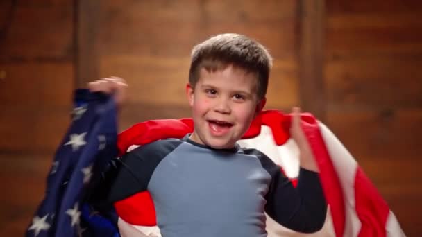 Ett leende barn viftar med Amerikas flagga. Mot en trä bakgrund, pojke visar patriotism — Stockvideo