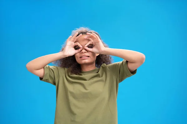 Αστεία νεαρή κοπέλα με αστεία χειρονομία πιλότου Αφρο-Αμερικανίδα γυναίκα κοιτάζοντας θετικά στην κάμερα φορώντας όμορφα t-shirt δείχνει τους μυς της απομονώνονται σε μπλε φόντο. Έννοια ομορφιάς — Φωτογραφία Αρχείου