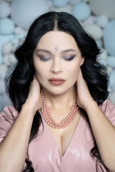 Kaukázusi csinos nő csukott szemmel tegye a kezét a tarkójára. Egy szexi barna arcú hölgy portréja. Közelkép. Pasztell labdák háttér — Stock Fotó