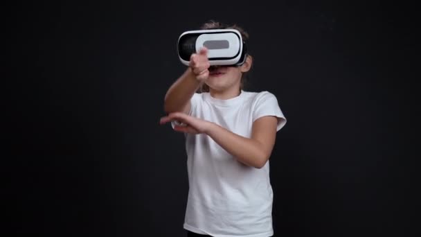 幸せな10歳の女の子は黒を背景に3Dで仮想現実の眼鏡で彼女の腕を振っています。白人の子供が来て、熱狂的に演奏します。高品質4k映像 — ストック動画