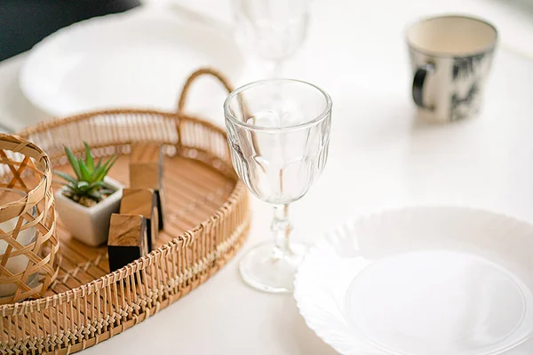 Serviert und dekoriert weißer Tisch mit Gläsern, Tellern und einem Becher. Tischdekoration mit Wicker und Holzdekor-Elementen — Stockfoto