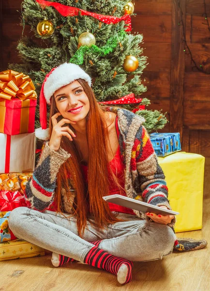 Beautiful Woman in a Winter Knitted Sweater, Hat and Striped Socks Κάθεται στο πάτωμα με σταυρωμένα πόδια Κοντά σε ένα σωρό από δώρα και ένα χριστουγεννιάτικο δέντρο. Κοντινό πλάνο — Φωτογραφία Αρχείου
