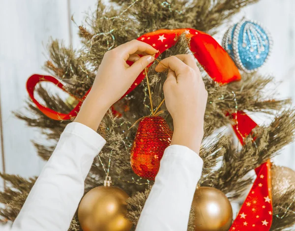 As mãos de crianças penduram uma decoração na árvore de Natal. Criança Decora a Árvore de Natal. Árvore de Natal Decorada com Fitas Vermelhas, Bolas Douradas, Serpentina. Close-up — Fotografia de Stock