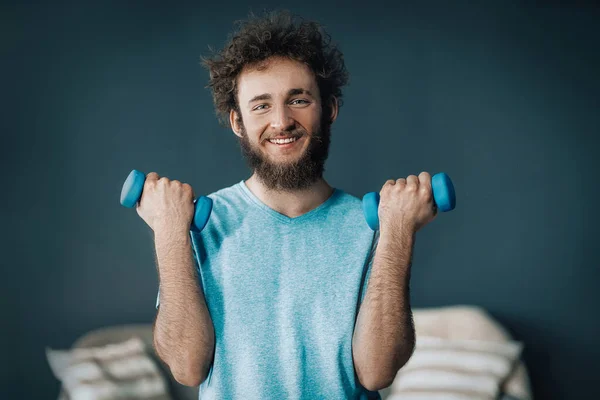 Hombre guapo hace ejercicio con pesimistas en casa. Guy se mantiene en forma durante la cuarentena. Fondo gris — Foto de Stock