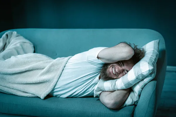 Lazy Guy vägrar att gå upp tidigt på morgonen för arbete. Man ligger på soffan täckt med en filt hemma. Närbild. — Stockfoto