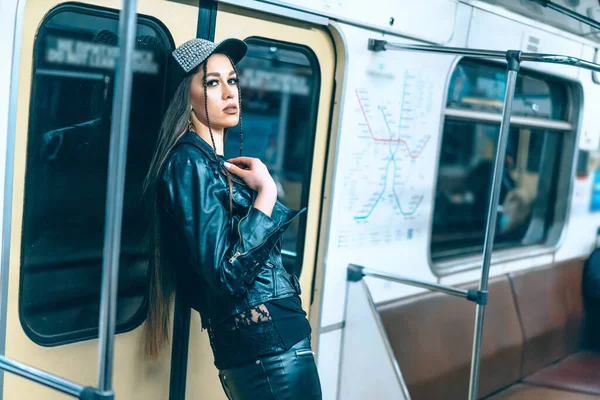 Sexig kvinna i stilrena kläder med långt brunt hår står vid dörren i en tågbil. Glamorös kvinna i tomma tunnelbanetåg. Närbild — Stockfoto