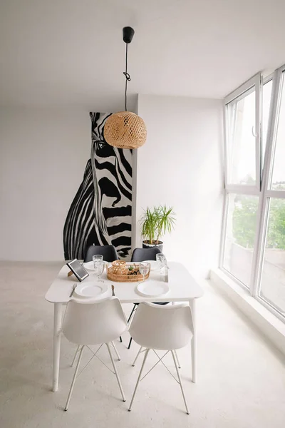 Interior Design of a Light Dining Room in a Minimalist Style with a Square Wooden Server Λευκό Τραπέζι, Μαύρες και Λευκές Καρέκλες, με Ψάθινες Διακοσμήσεις στον Πολυέλαιο και στο Τραπέζι. — Φωτογραφία Αρχείου