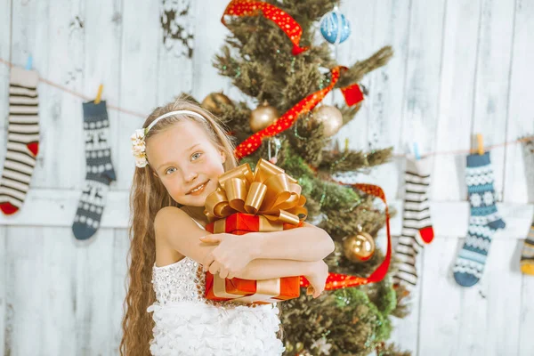笑顔の女の子は彼女の手の中にリボンと緑豊かな黄金の弓を持つ赤い正方形のクリスマスギフトボックスを保持しています。クリスマスと新年の祝日。閉鎖 — ストック写真