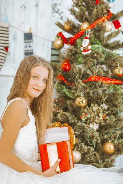 ツツのドレスのブロンドの若い女性は装飾されたクリスマスツリーの下の床に座り、彼女の手にオープンレッドギフトボックスを保持します。閉鎖 — ストック写真