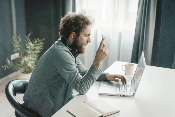 A fiatal üzletember elemzi az új online üzleti stratégiákat a karantén ideje alatt. Egy fiatalember ül az asztalnál egy csésze kávéval és gépelési szöveggel a laptopján. Közelkép — Stock Fotó