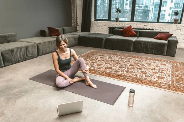 Sporty Woman Sits on a Sport Mat and Has an Online Video Chat with her Fitness Coach on Laptop During the Quarantine Period. Home Workouts. City Background. Close-up — Foto Stock