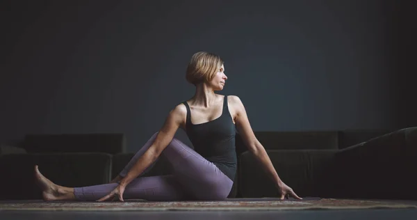 Yoga class. A beautiful, trained body. Woman makes an asana against a dark background in a city apartment. Body beauty concept. — Fotografia de Stock