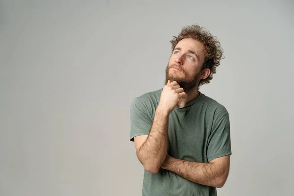 Dreamy Curly Guy guarda allo spazio di copia, Thoughtful Man pensa al suo futuro. Modello Maschio in Grafite T-shirt Posa in Studio con fondo grigio chiaro. Primo piano — Foto Stock