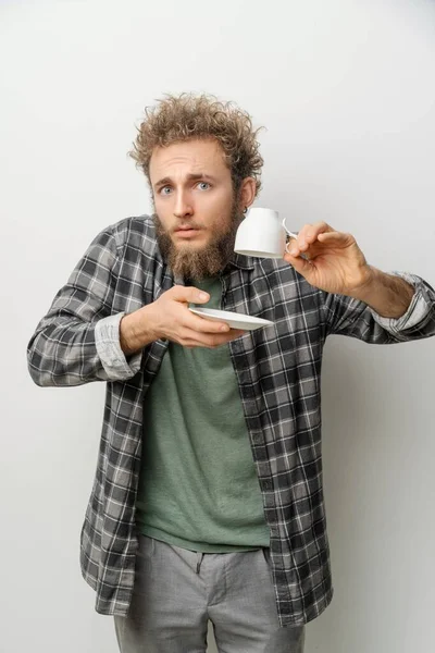 Young guy with an inverted and empty cup and saucer in his hands. Concept of where my coffee is, to last drop. That was last straw of my patience. — Stock Photo, Image