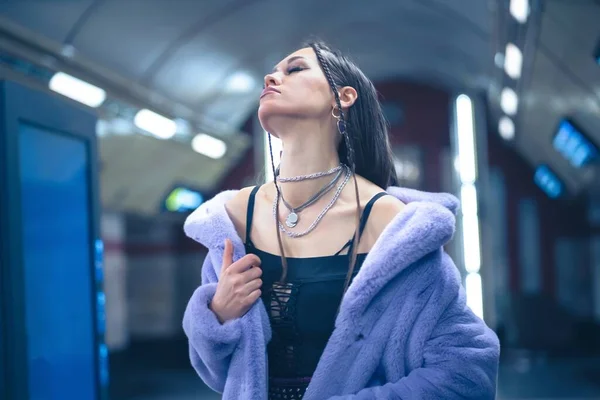 Σέξι μοντέλο σε μωβ συνθετικό γούνινο παλτό με τα πόδια στο μετρό ή πλατφόρμα του μετρό σε μπλε φόντο. Γυναικείο με πολυτελές μακιγιάζ, μακριά μαλλιά σε κομψό ντύσιμο — Φωτογραφία Αρχείου
