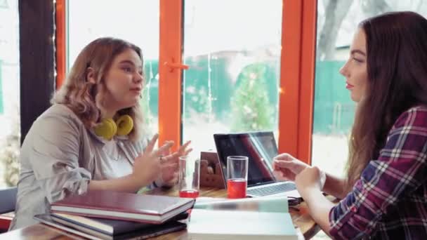 Nahaufnahme zweier Studentinnen im ersten Semester, die sich in einem Café unterhalten und ihre Geschichten erzählen, während im Hintergrund Lichter laufen und offene Bücher und Laptop auf dem Tisch liegen. 4K-Filmmaterial Stock-Filmmaterial