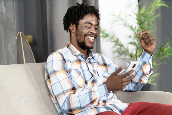Homem positivo em roupas casuais Sentado no sofá e assistindo memes engraçados em seu smartphone. Cara engraçado rindo e olhando para a tela de seu dispositivo móvel no sofá. Close-up — Fotografia de Stock