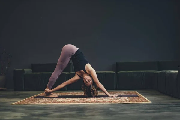 Smiling young woman on a mat does an asana. Concept of yoga in the city. Health, longevity, slim figure. — Foto Stock