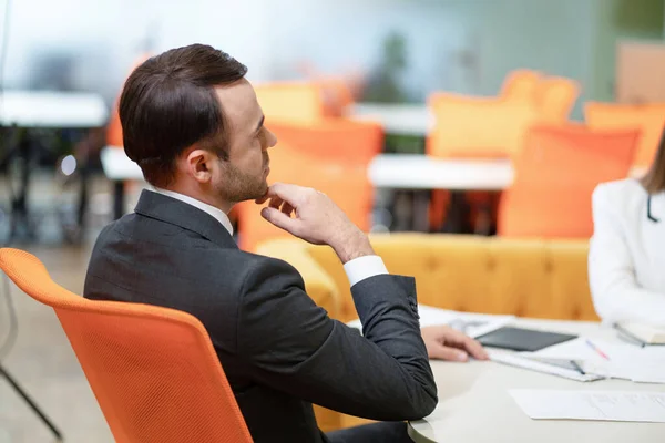 Elegante Empresario se sienta de nuevo a la cámara en una silla naranja y escucha un informe sobre el trabajo realizado, Propuestas para mejorar el negocio. Vida de oficina. Día de trabajo. —  Fotos de Stock