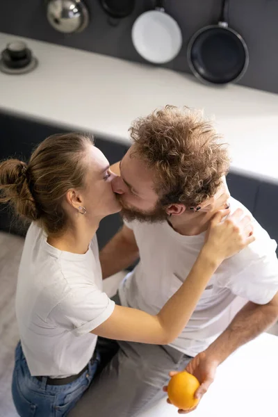 Beijando belo casal abraçando uns aos outros, em sua nova casa. Divirta-se na cozinha moderna e beije enquanto cozinha em casa. Conceito de uma nova casa — Fotografia de Stock