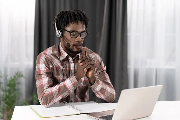 Afrikai szabadúszó nézi a laptopot fejhallgatóval, miközben egy csoportos videohívás távolról dolgozik otthon. Fiatal diák a távolban hajlik van egy videócsoport hívás. Távoktatási koncepció — Stock Fotó