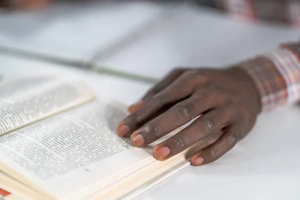 Закройте руку африканского американца на открытой книге. Студент готовится к лекции в библиотеке, читает книги и делает заметки. Концепция добавления — стоковое фото