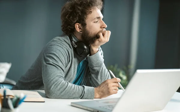 Op afstand werken, een dure jongeman die thuis werkt. Ernstige jonge freelancer zitten aan de balie en met behulp van laptop op kantoor en het maken van aantekeningen. Werk vanuit huis concept — Stockfoto