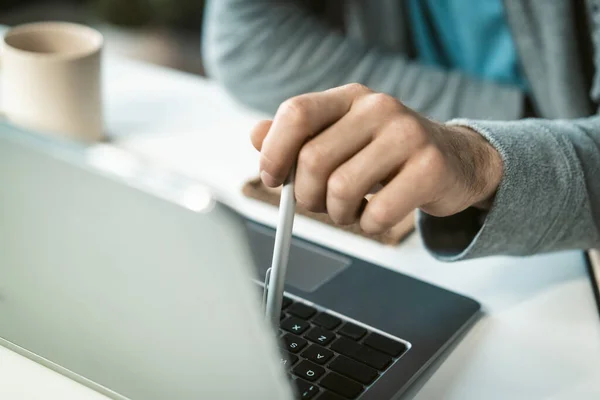 Homem freelancer close-up trabalhando no laptop sentado na mesa em casa digitando usando uma caneta. Jovem trabalhador remoto e pensativo que trabalha em casa. Trabalho a partir de casa conceito — Fotografia de Stock