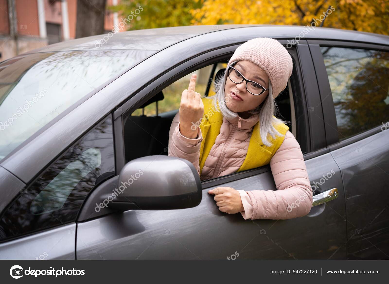 Angry asian woman showing middle finger or fuck leaning out the car window.  Mature asian woman
