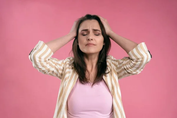 Estresado o tener una mujer de negocios con dolor de cabeza en traje sosteniendo la cabeza con los ojos cerrados aislados en el fondo rosa. Mujer empleada estresada en traje de rayas —  Fotos de Stock