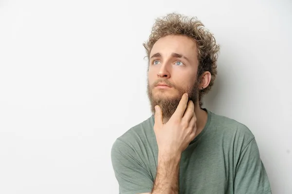 Gedachte of dure jonge knappe bebaarde wilde krullend haar man met heldere blauwe ogen geïsoleerd op witte achtergrond. Jonge denkende man in groen tshirt op wit — Stockfoto