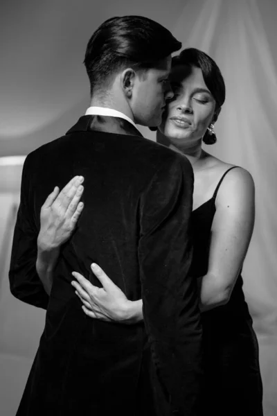 Pasión en el amor mujer abraza hombre de pie detrás de la cámara. Marido y esposa después de una cena romántica. Romance en las relaciones. Hermosa pareja joven en el interior del hogar. Foto en blanco y negro —  Fotos de Stock