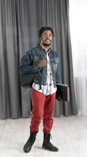 Trendig ung afrikansk-amerikansk man med skägg håller böcker och ryggsäck bär denim jacka redo att gå till studier. Stilig ung elev på väg till skolan. Skolbegreppet. Undersökningsidé — Stockfoto