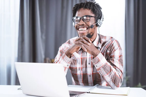 Heureux pigiste ou étudiant afro-américain travaillant à la maison en utilisant un ordinateur portable avec écouteurs pour un appel vidéo de groupe travaillant à distance. Jeune étudiant penché à distance ont un appel de groupe vidéo — Photo