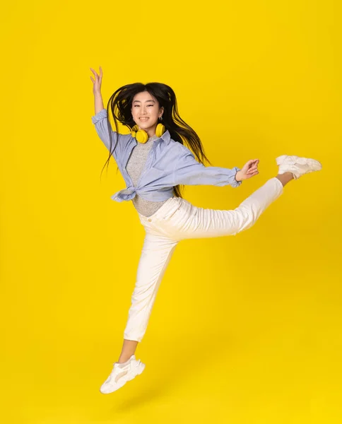 Młoda szczęśliwa dziewczyna skacze na żółtym tle. Azji młoda kobieta z długimi włosami mucha w stylu baleriny. — Zdjęcie stockowe