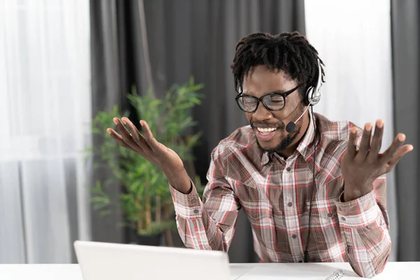 Gesturing african american freelancer looking at laptop with headphones having a group video call working distantly at home. Young student on distant leaning have a video group call — Foto Stock
